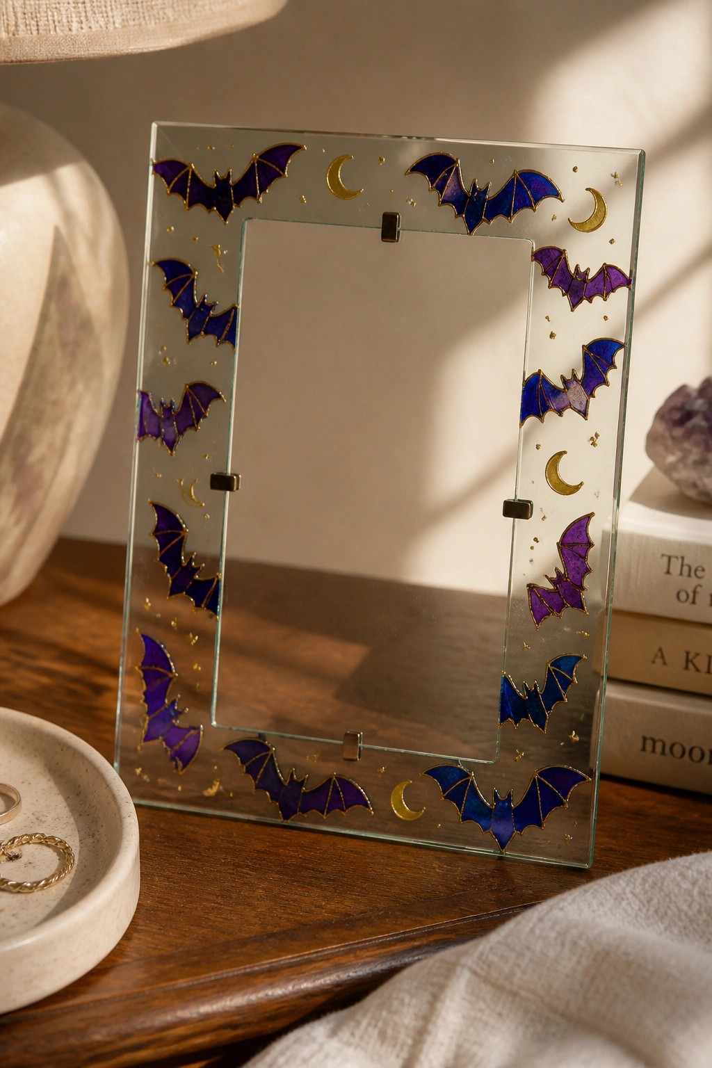 Glass photo frame with purple bats, gold moons and stars on wooden table.