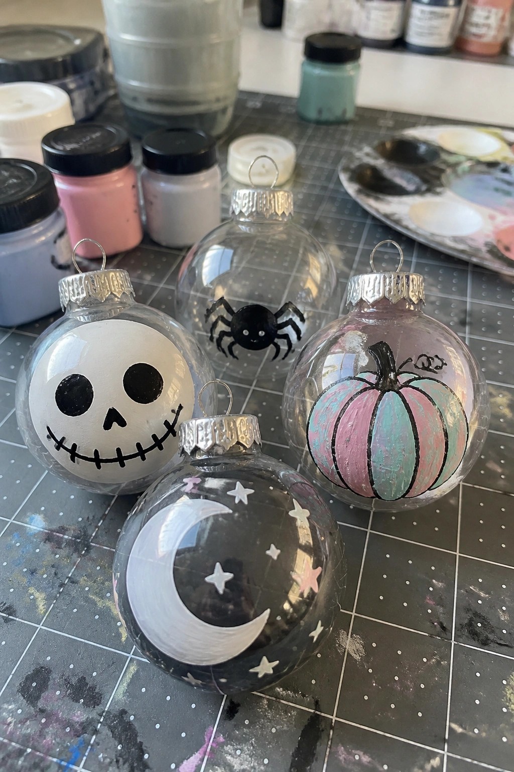 Four hand-painted glass ornaments with skull, spider, pumpkin, and moon designs on mat.
