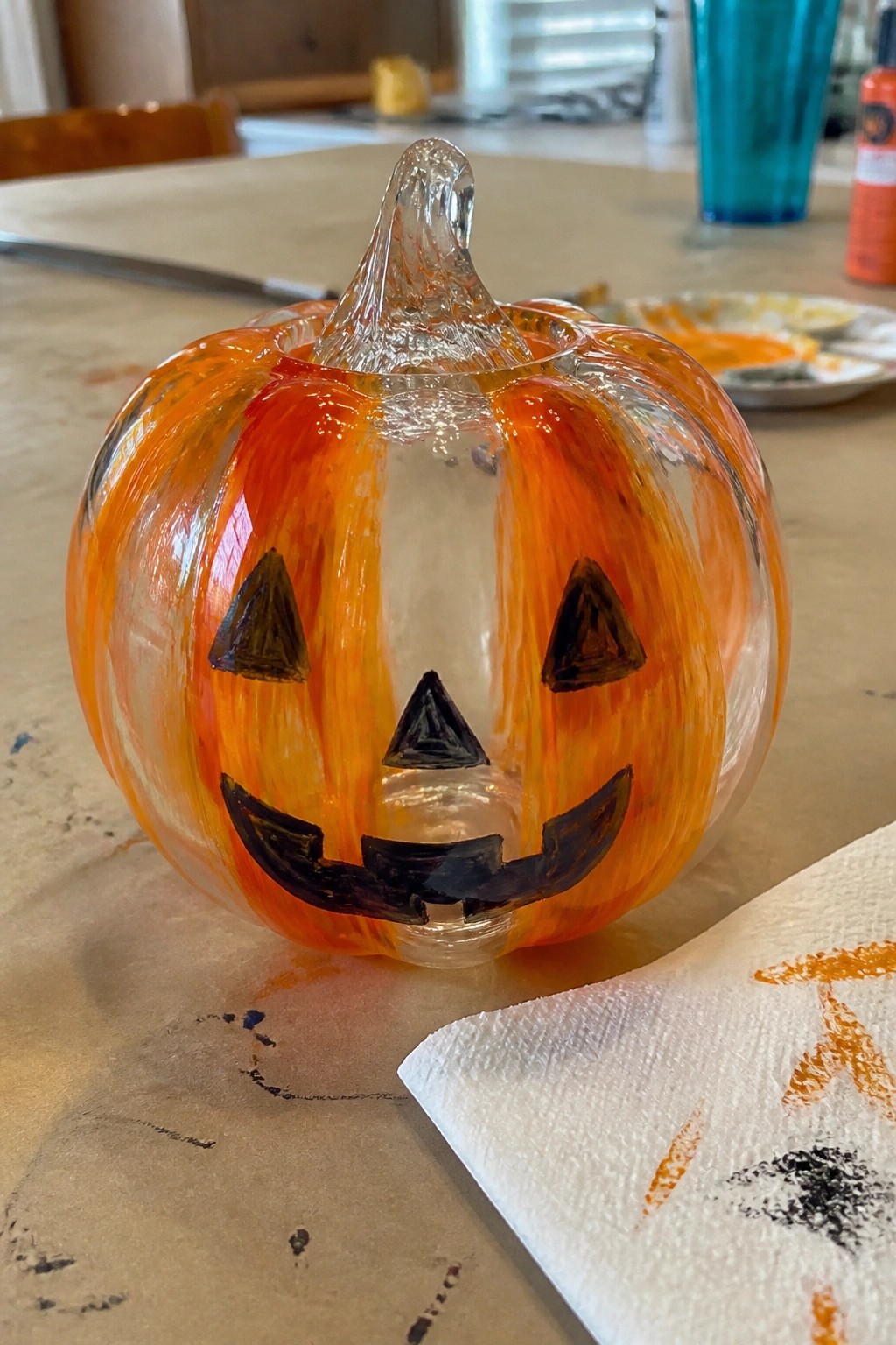 Clear glass pumpkin with orange brushstrokes and black jack-o'-lantern face on table