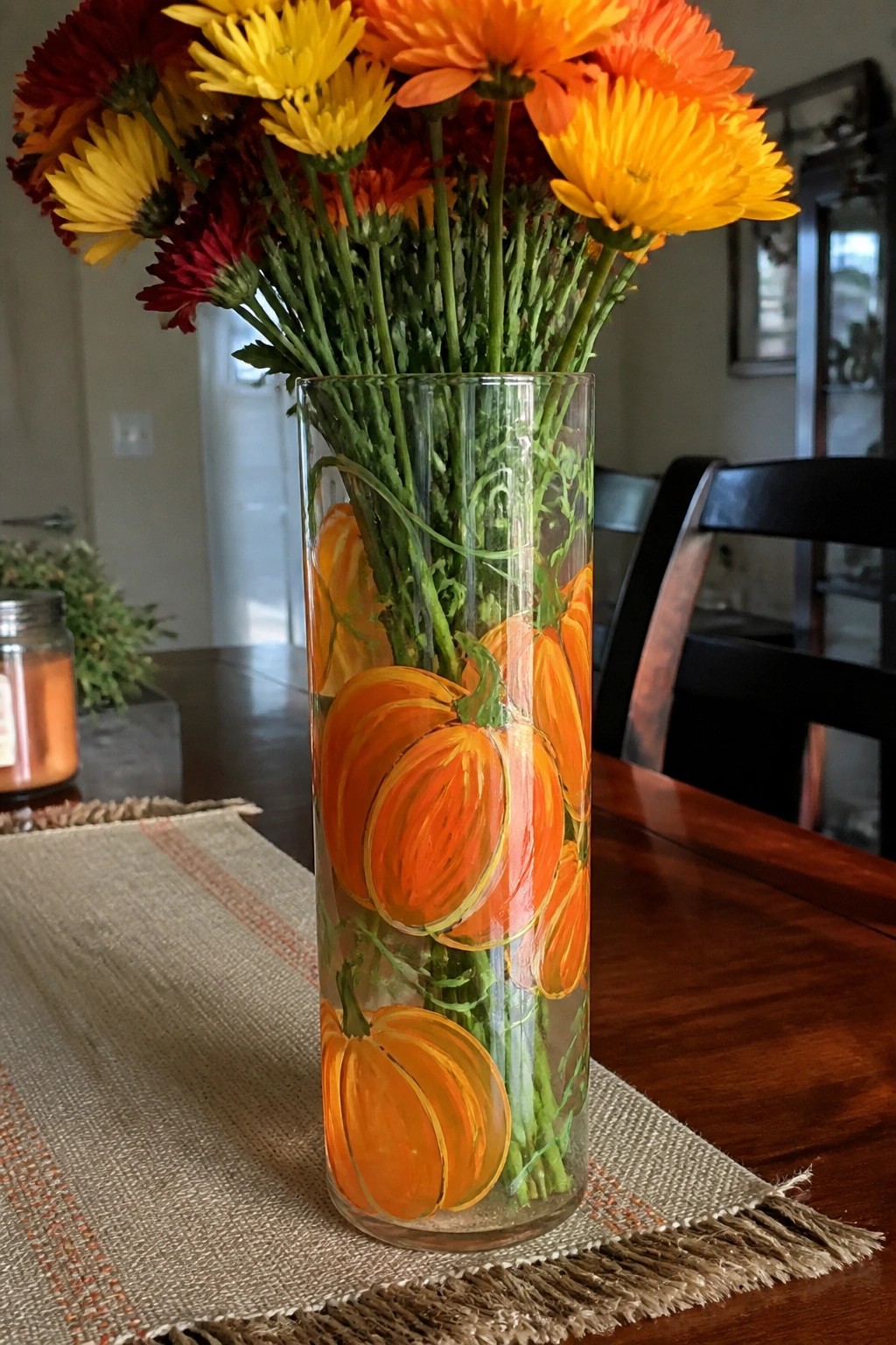 Clear glass vase with painted pumpkins holding vibrant yellow, orange, and red flowers.