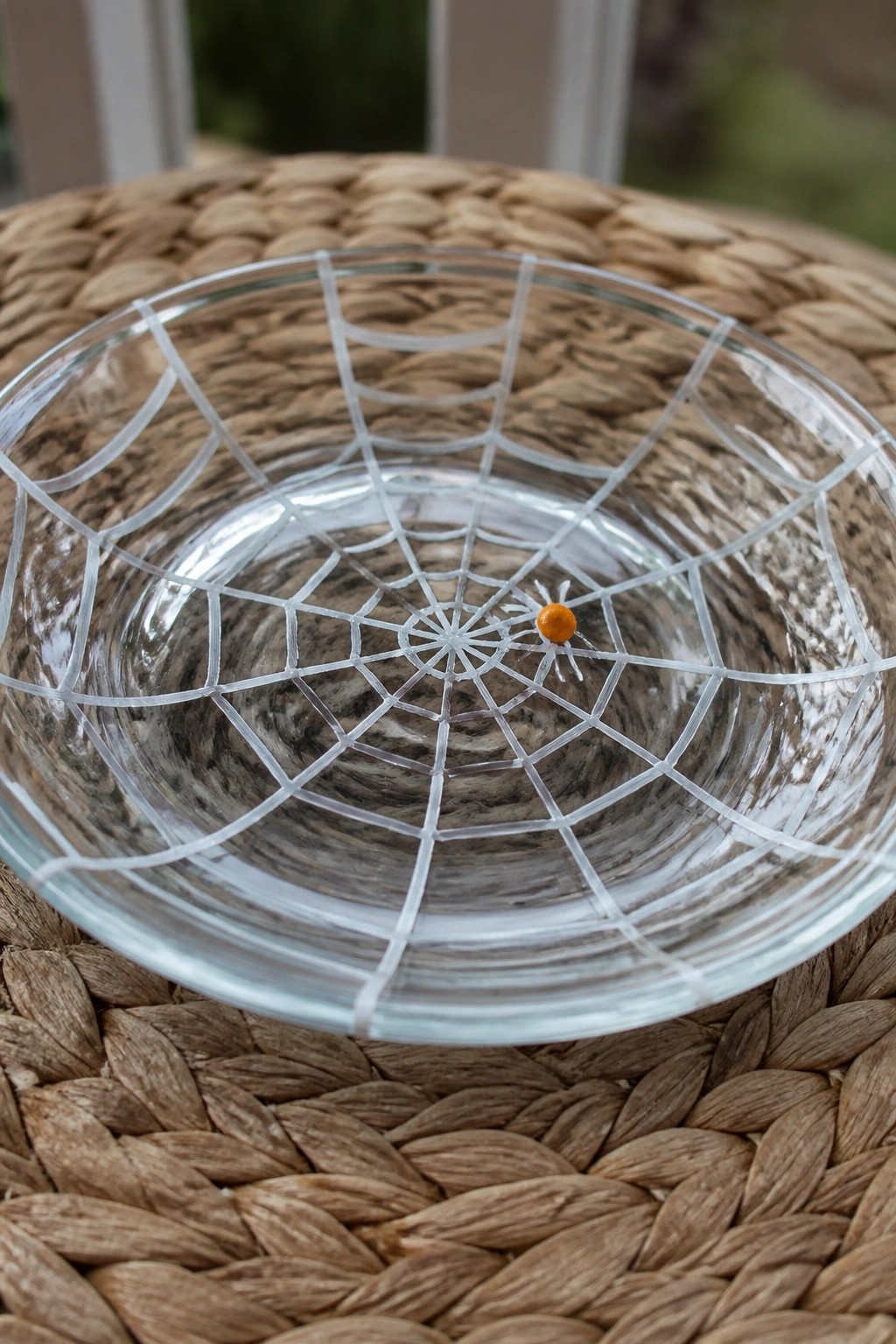 Glass bowl with white spiderweb and small orange spider on woven mat