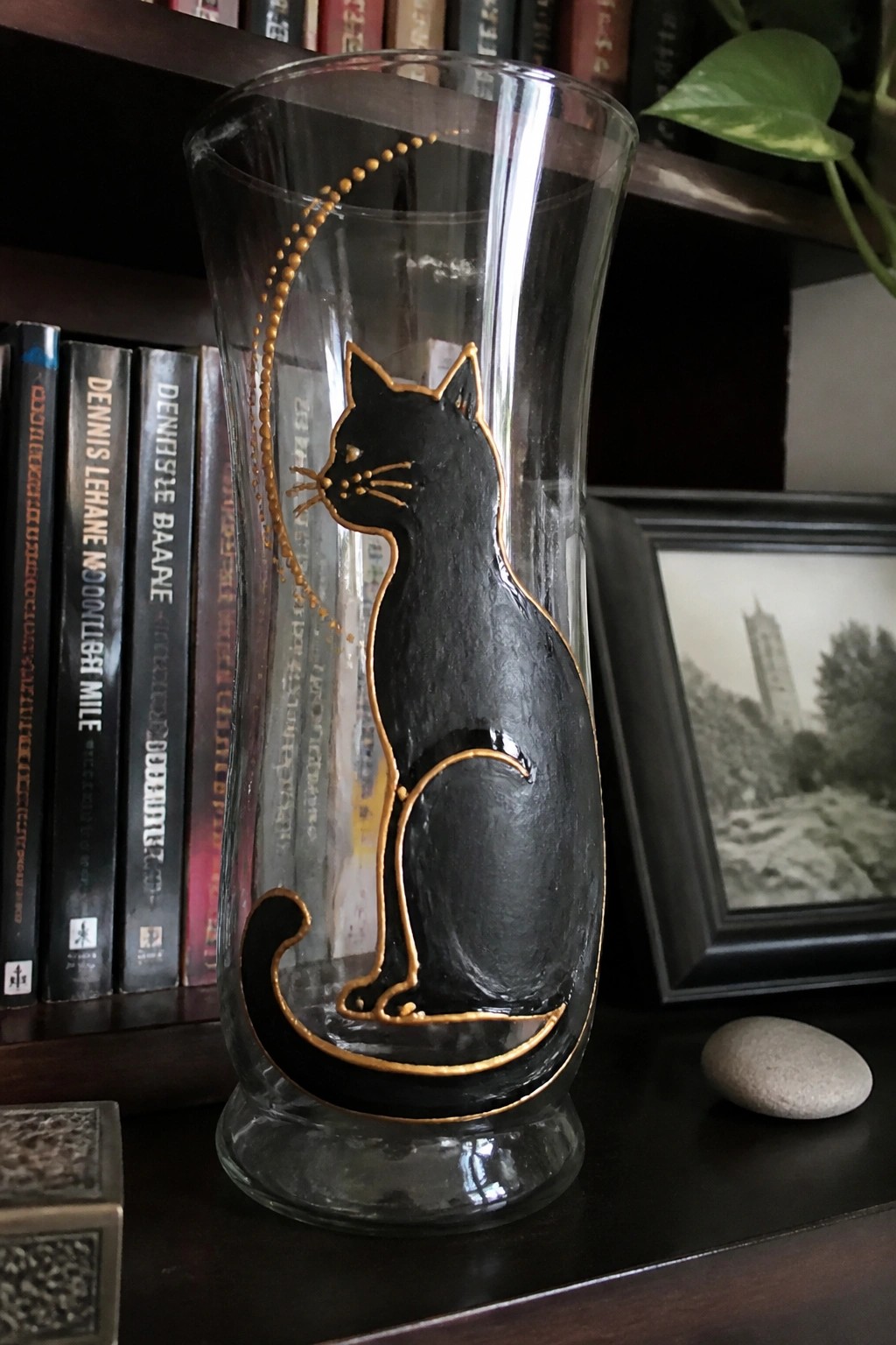 Black cat silhouette with gold outline on tall glass vase beside books.