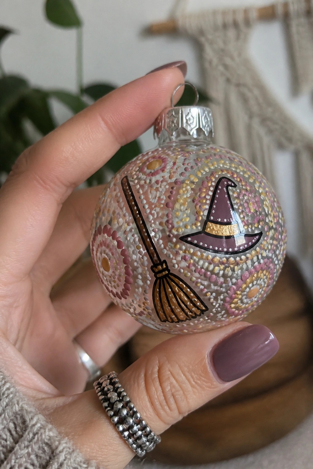 Hand holding dotted glass ornament with witch hat and broomstick.
