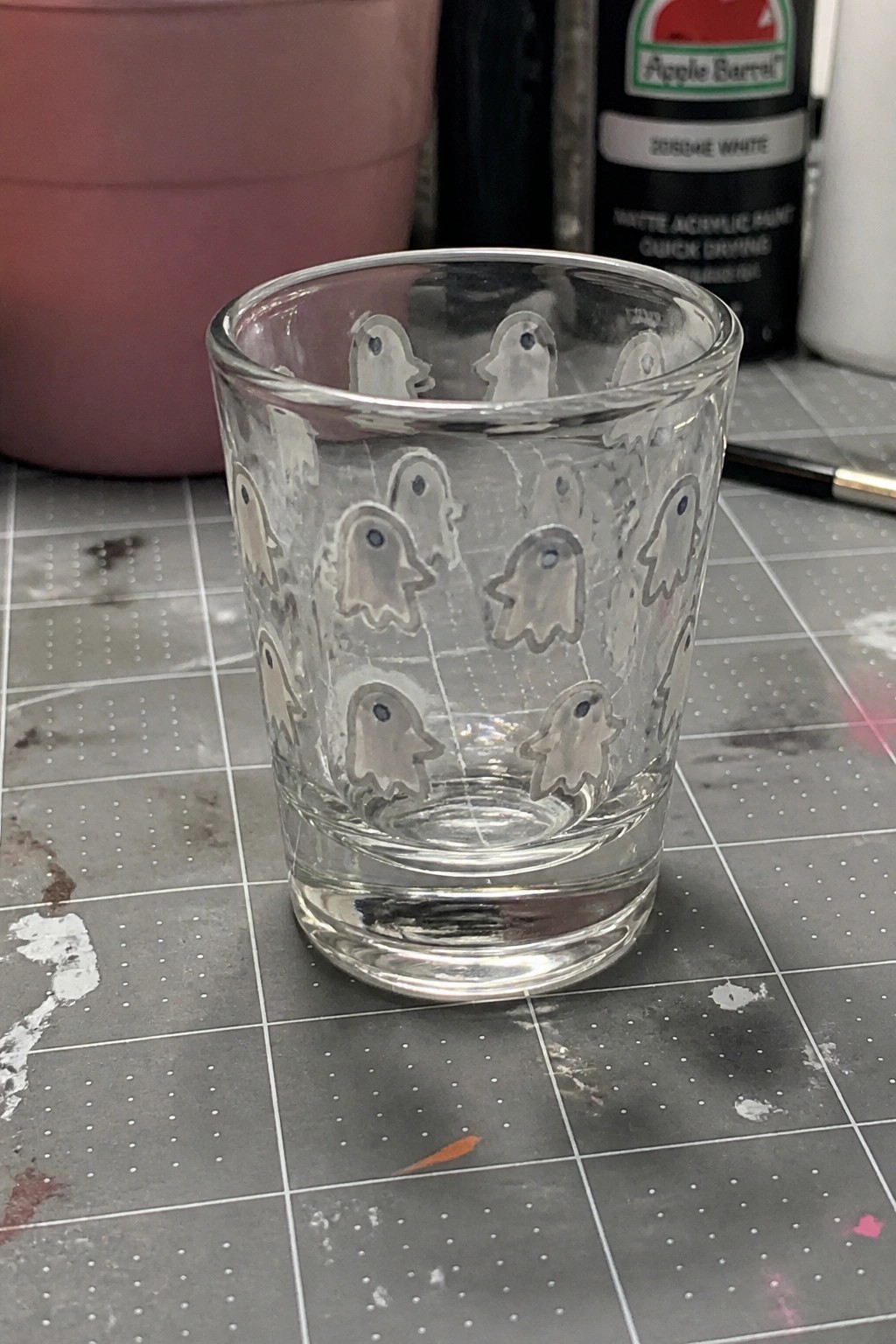 Small clear glass cup with white ghost designs on gridded cutting mat