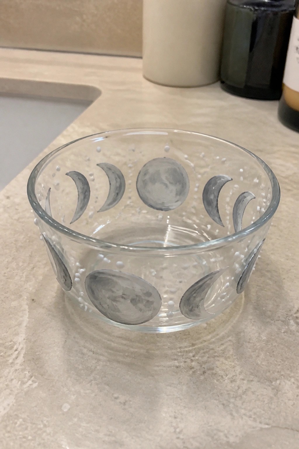 Clear glass bowl with gray painted moon phases and white dots on marble countertop