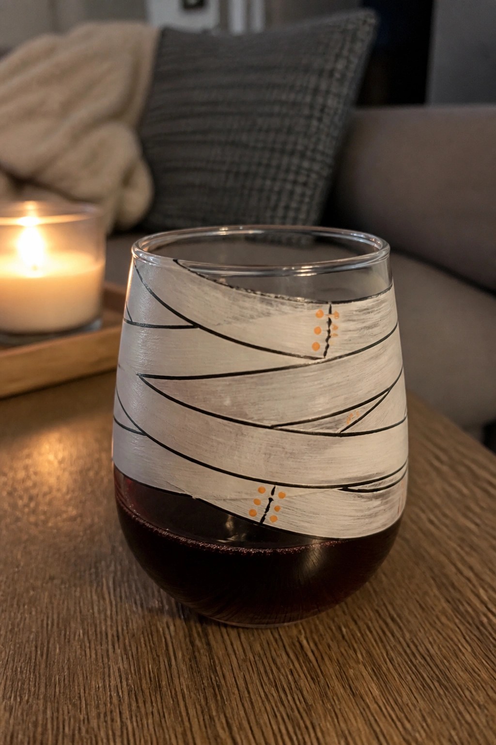 Stemless wine glass of red wine with white mummy wrap design on wooden table
