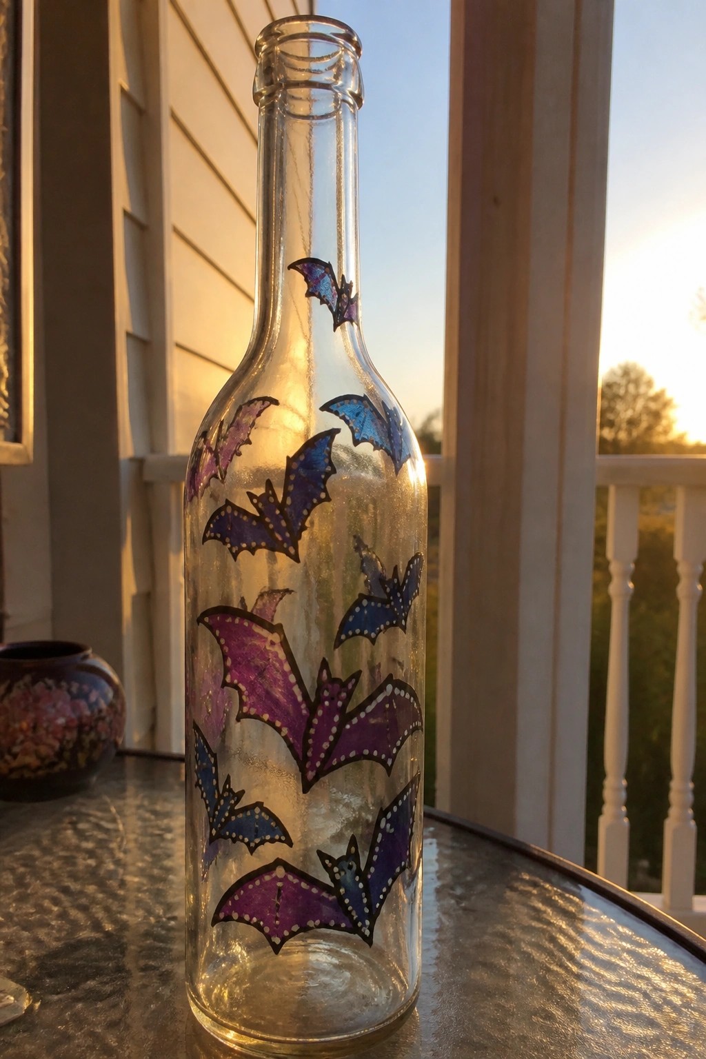 Glass bottle with purple and blue dotted bats on table at sunset