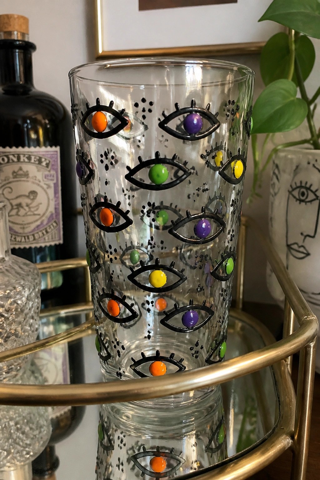 Clear glass tumbler covered in black-outlined eyes with colorful irises.