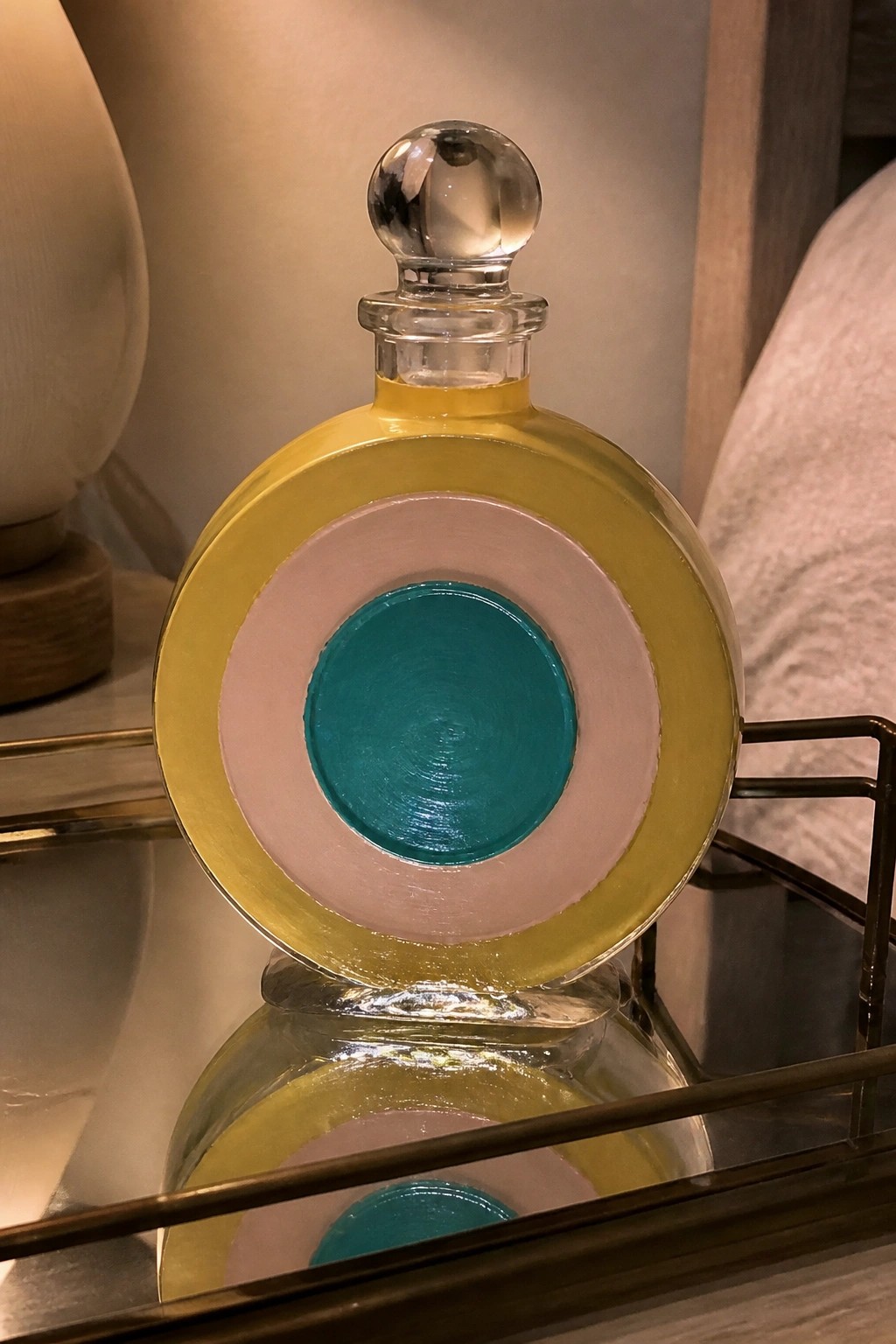 Round glass bottle with yellow, pink, and teal concentric circles on mirror tray.