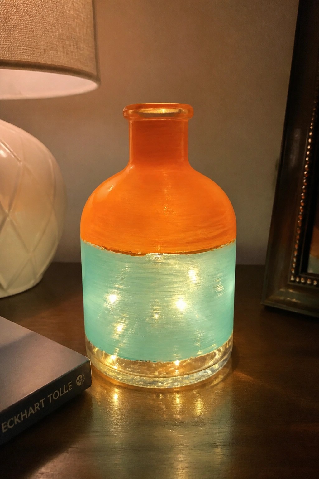 Glowing orange and turquoise painted glass bottle on dark wooden table