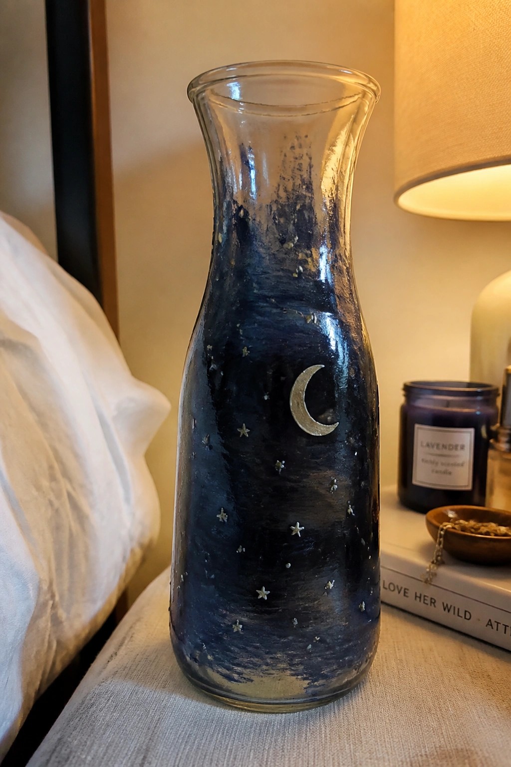 Dark blue glass vase with moon and stars on bedside table beside lamp