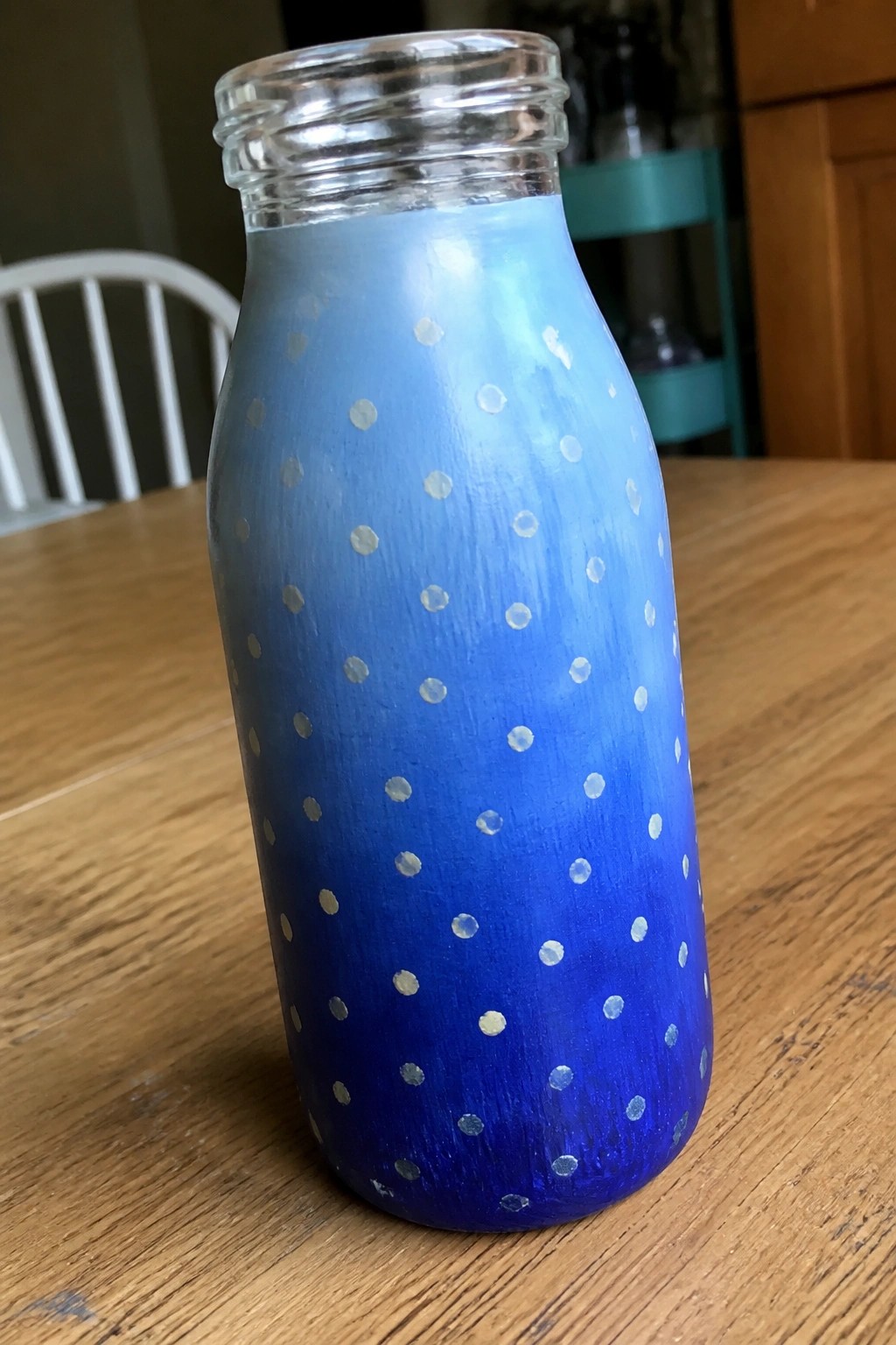 Blue gradient glass bottle with white dots on wooden table.