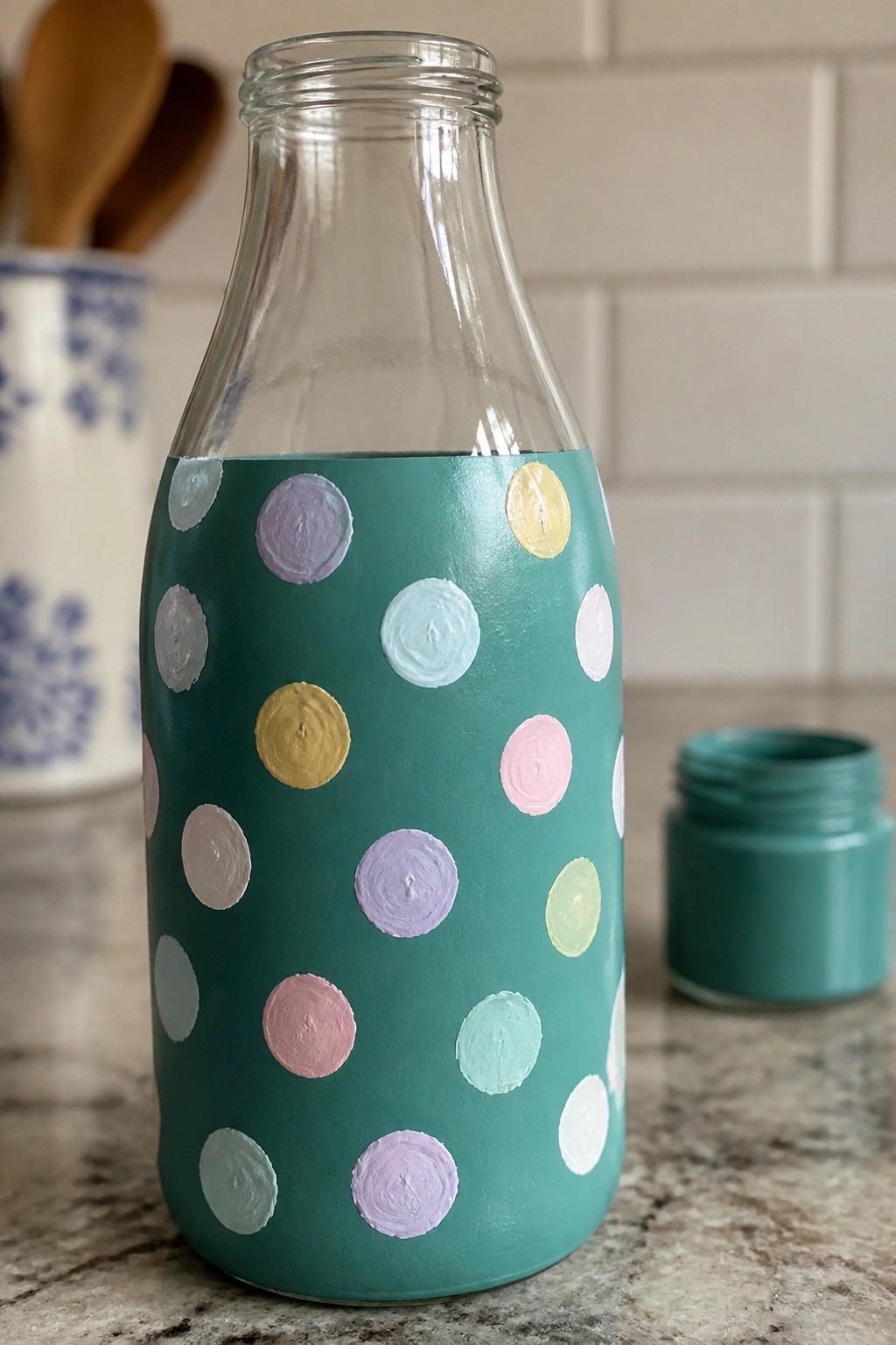 Teal-painted glass bottle with pastel polka dots beside open paint jar.
