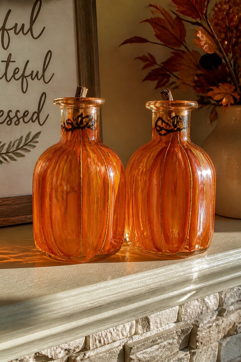 Two orange glass pumpkin vases with gold lines on a white mantel.