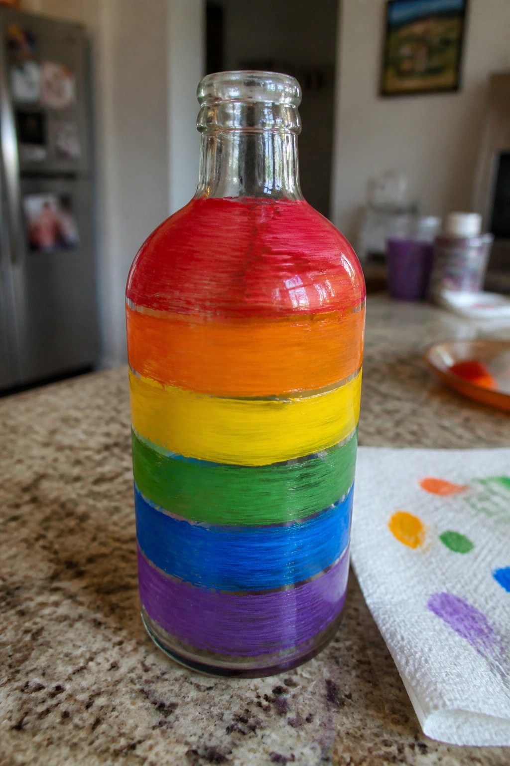 Glass bottle with red orange yellow green blue purple horizontal paint stripes on counter