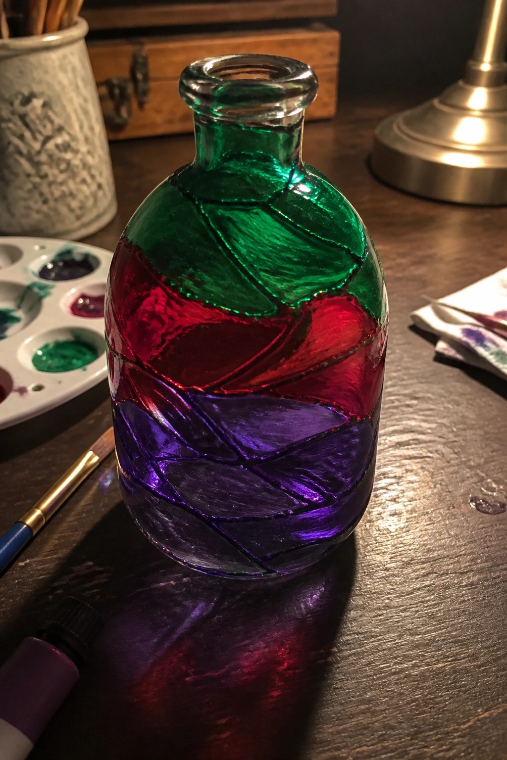 Painted glass bottle with swirling green, red, and purple sections on wooden table