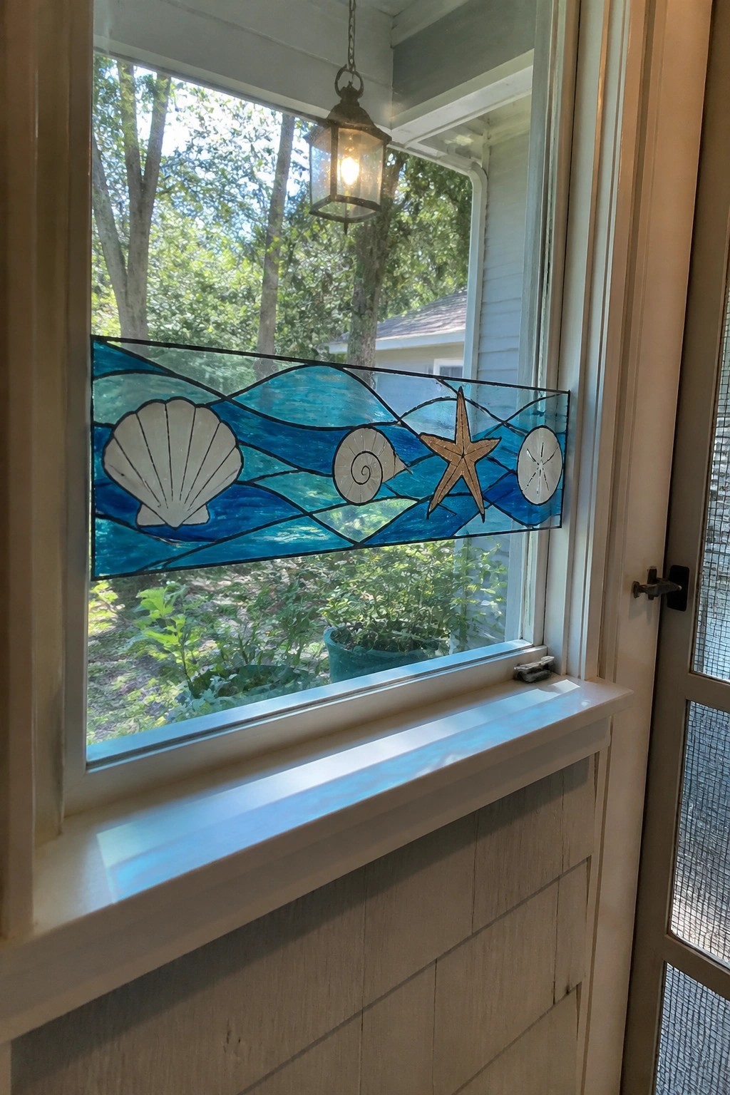 Stained glass panel with blue waves, seashells, starfish, and sand dollar in window
