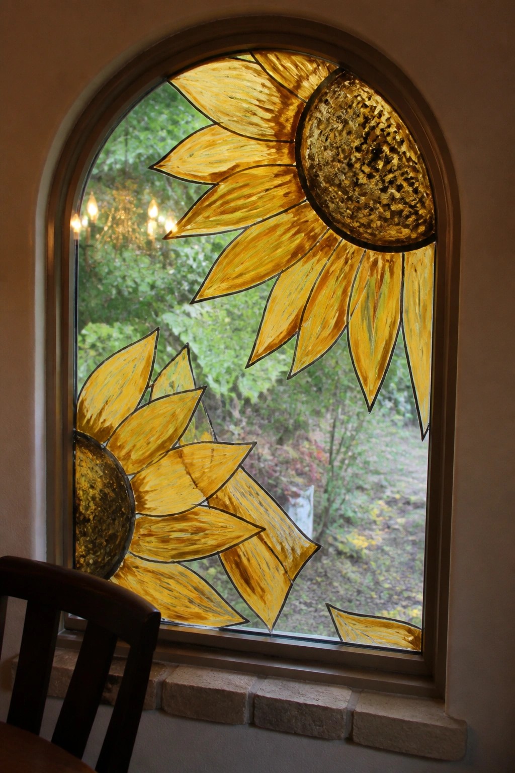 Arched window featuring vibrant yellow stained glass sunflowers with green foliage visible beyond.