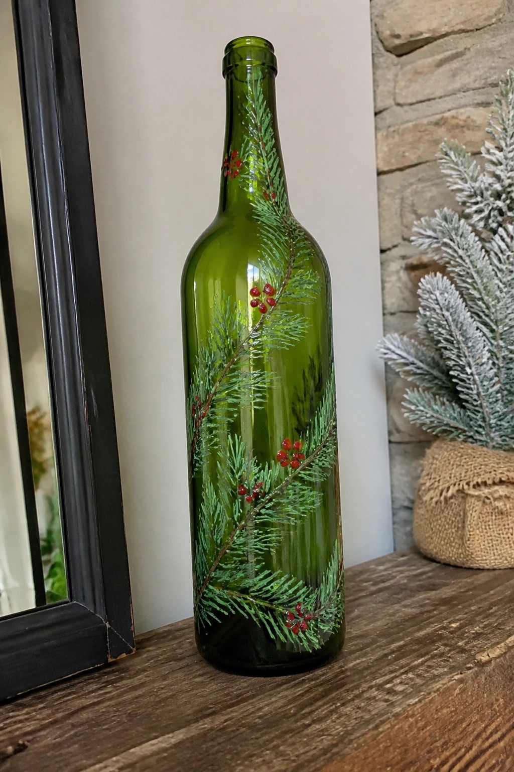 Green glass bottle painted with pine branches and red berries on wooden table