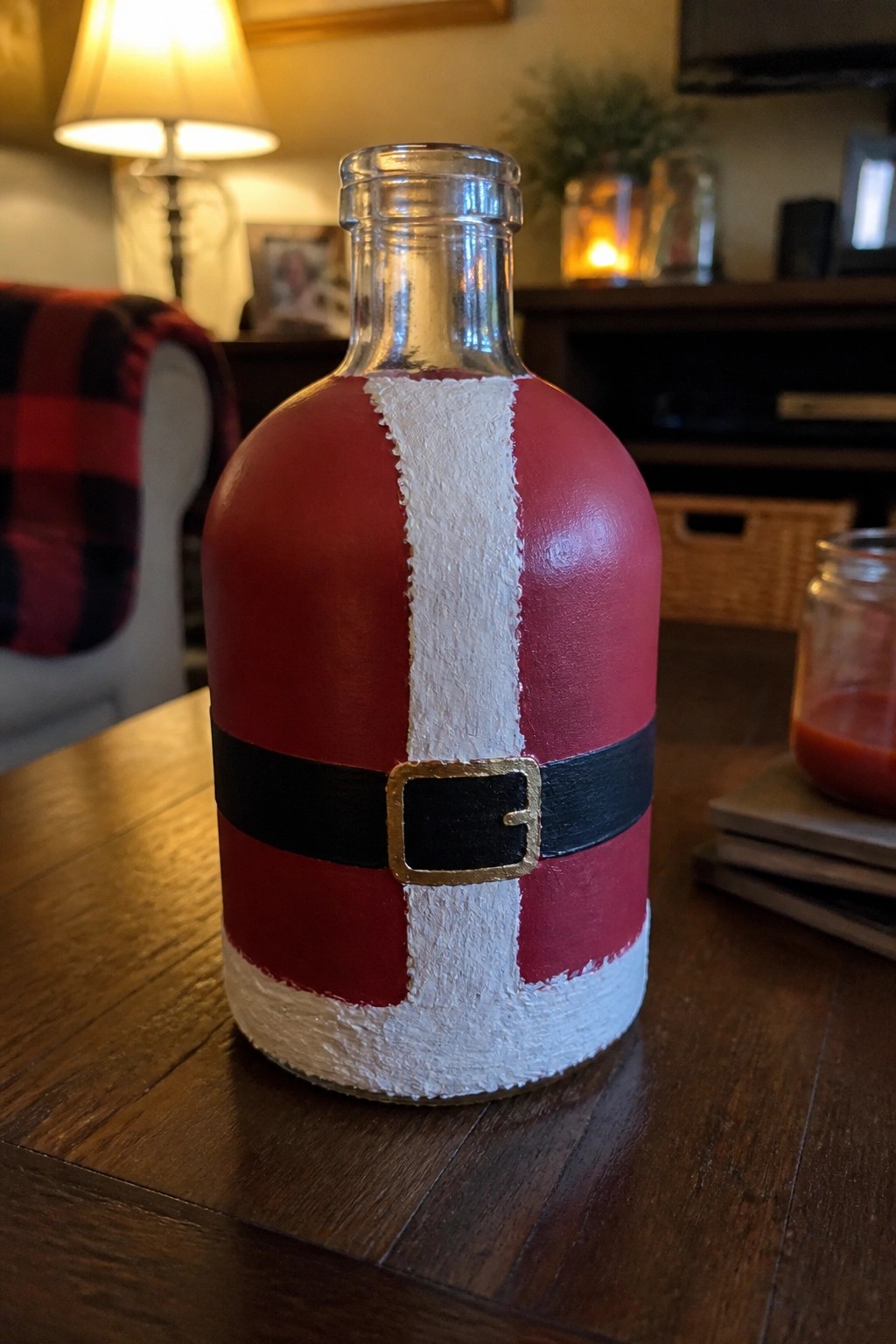 Santa Claus-themed painted bottle in red with white stripe and black belt on table.
