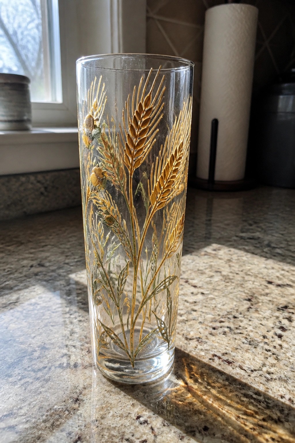 Tall glass with golden wheat stalks on speckled granite countertop