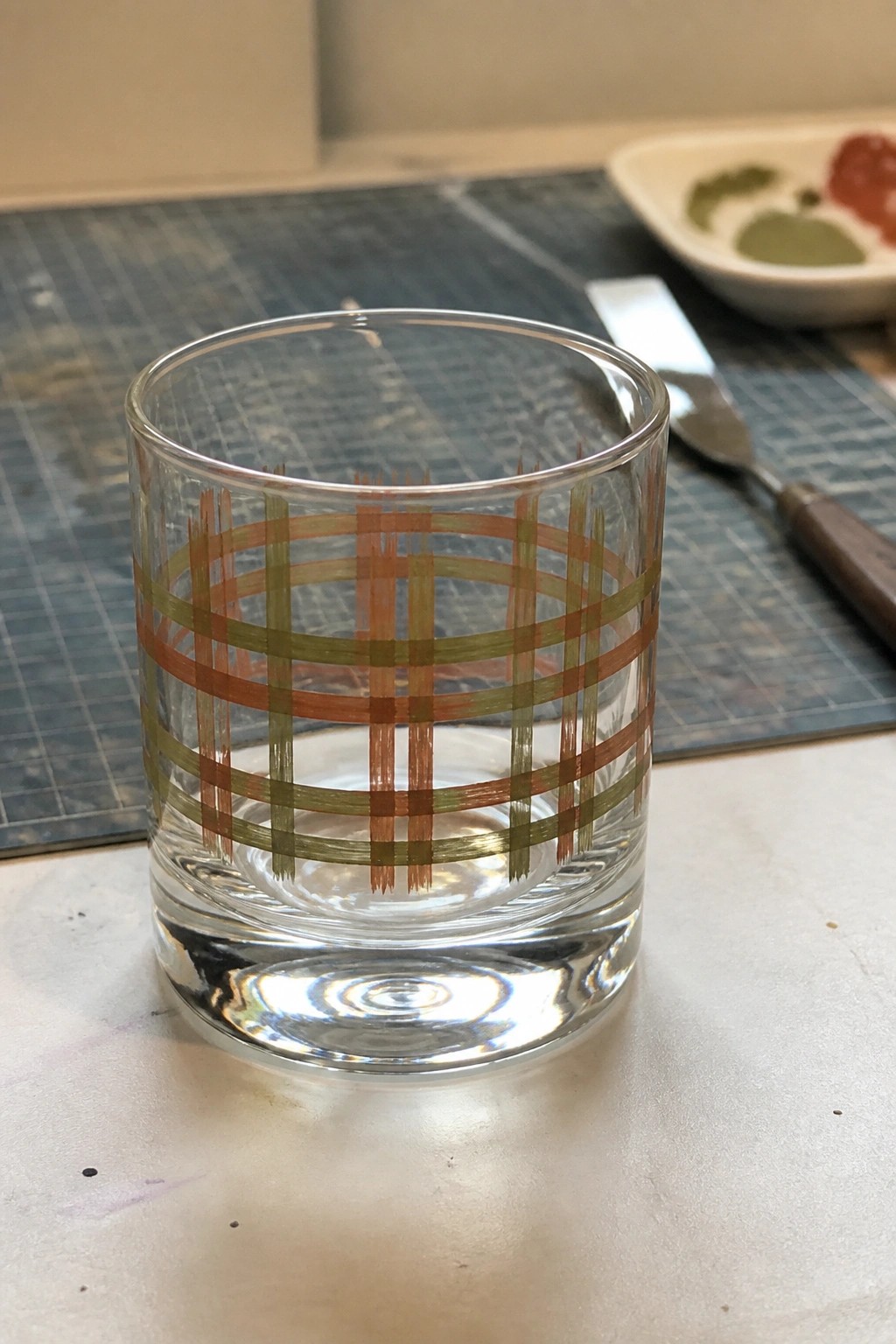 Clear glass tumbler with hand-painted green and orange plaid pattern on white surface