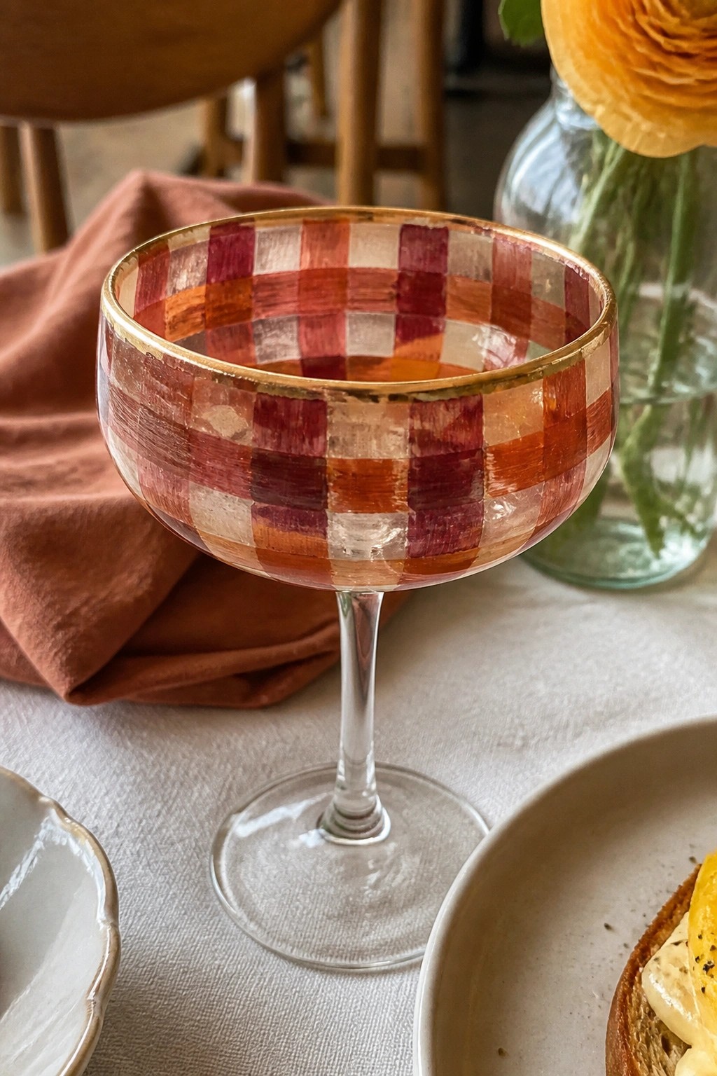 Checkered red-orange coupe glass with gold rim on white tablecloth