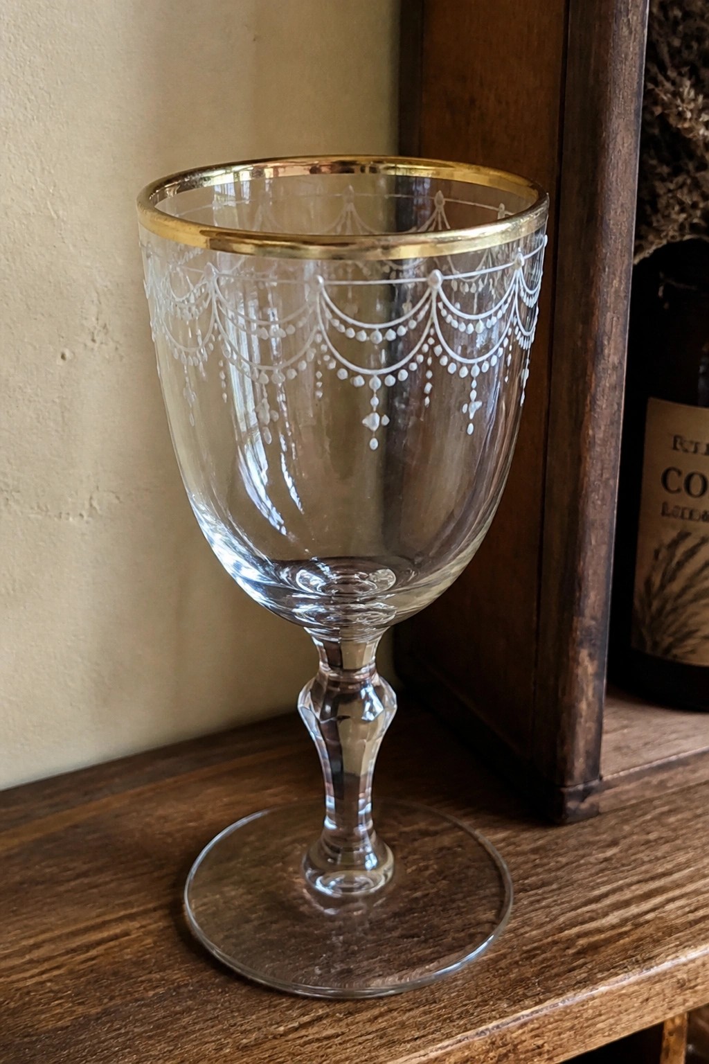 Ornate crystal goblet with gold rim and white etched garland design on wood