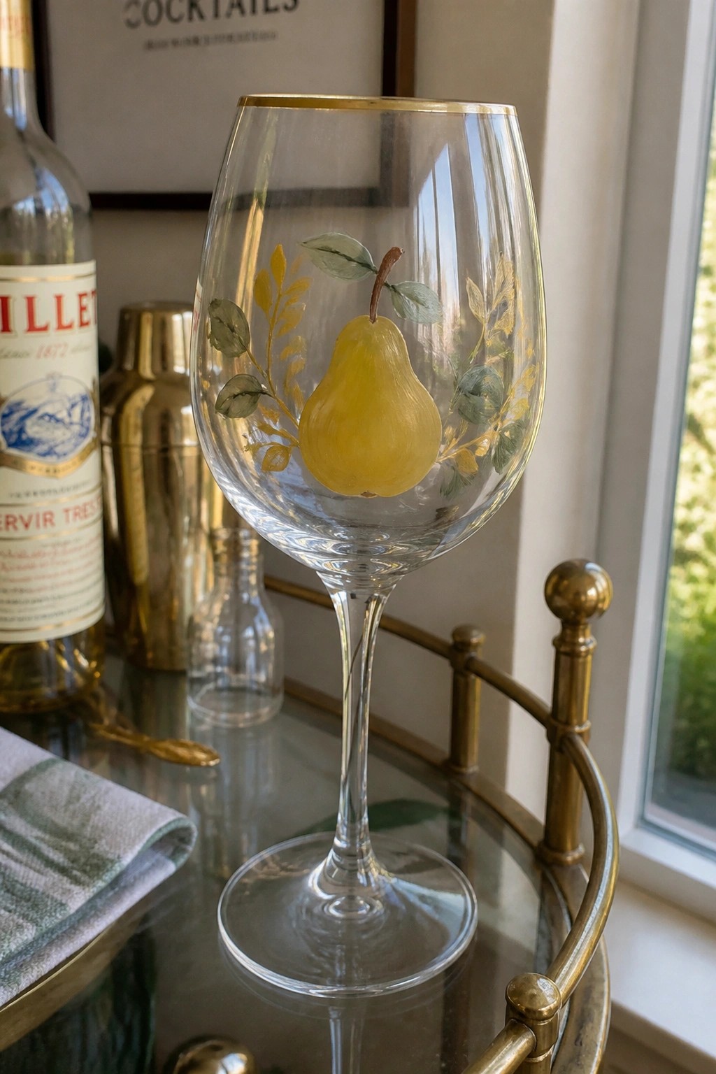 Wine glass with hand-painted yellow pear, green leaves, and gold rim on bar cart