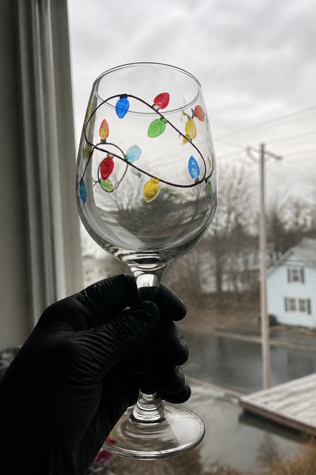 Black-gloved hand holds wine glass painted with colorful Christmas lights.