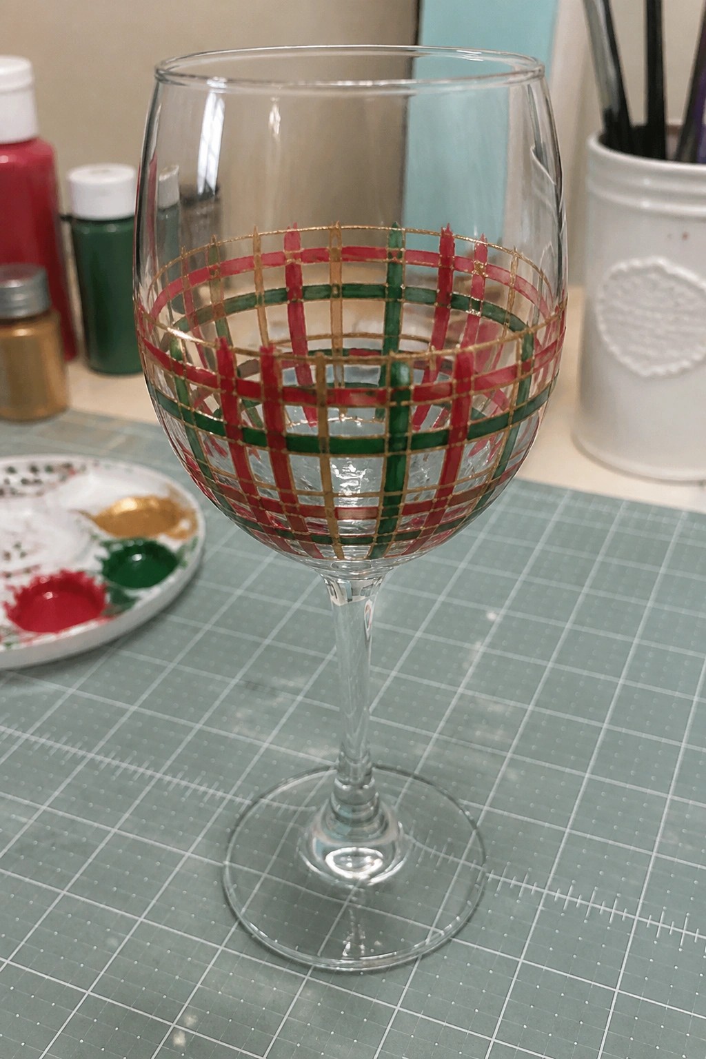 Wine glass with red green gold plaid design on green cutting mat