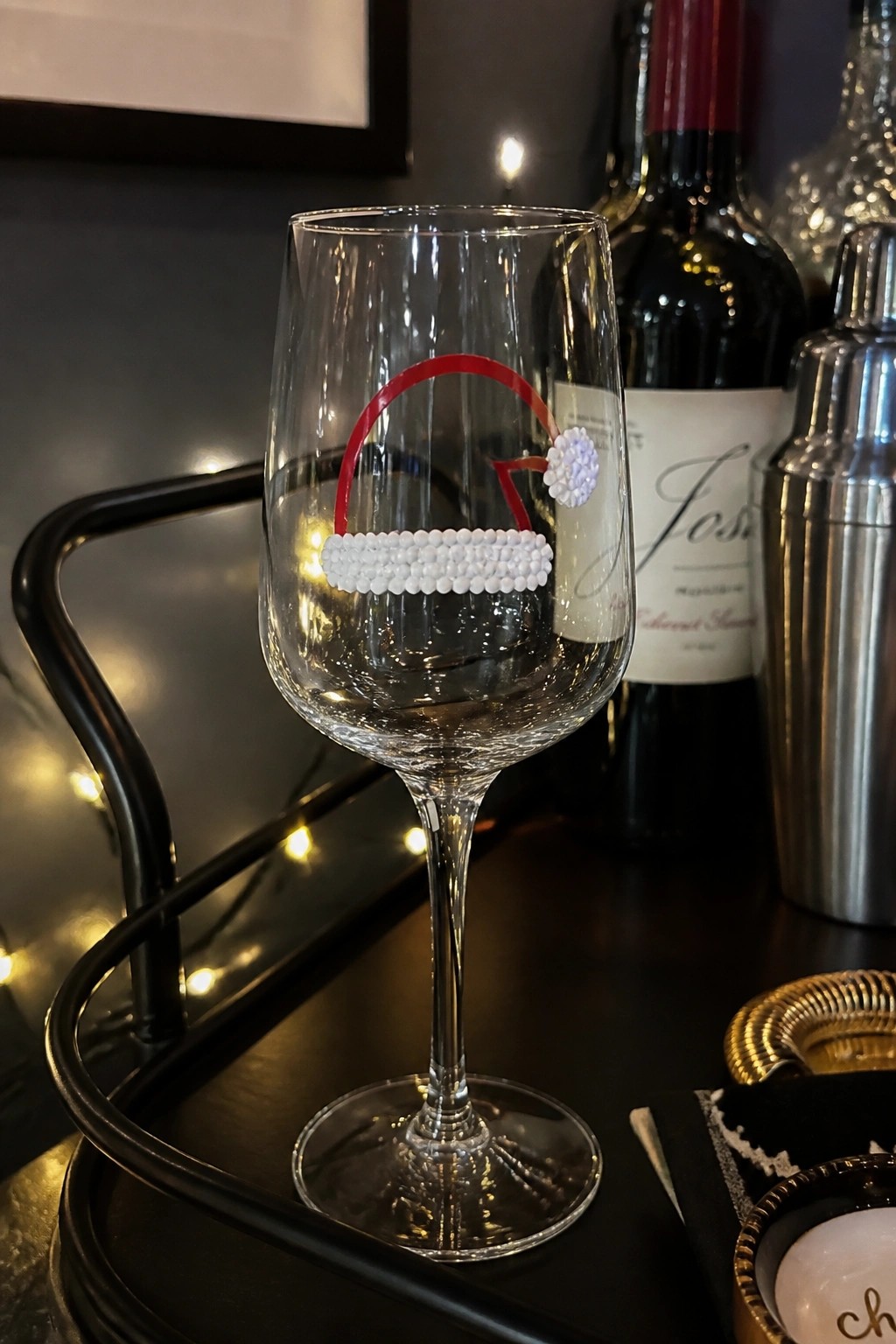 Wine glass with red-and-white beaded Santa hat decoration on dark tray.