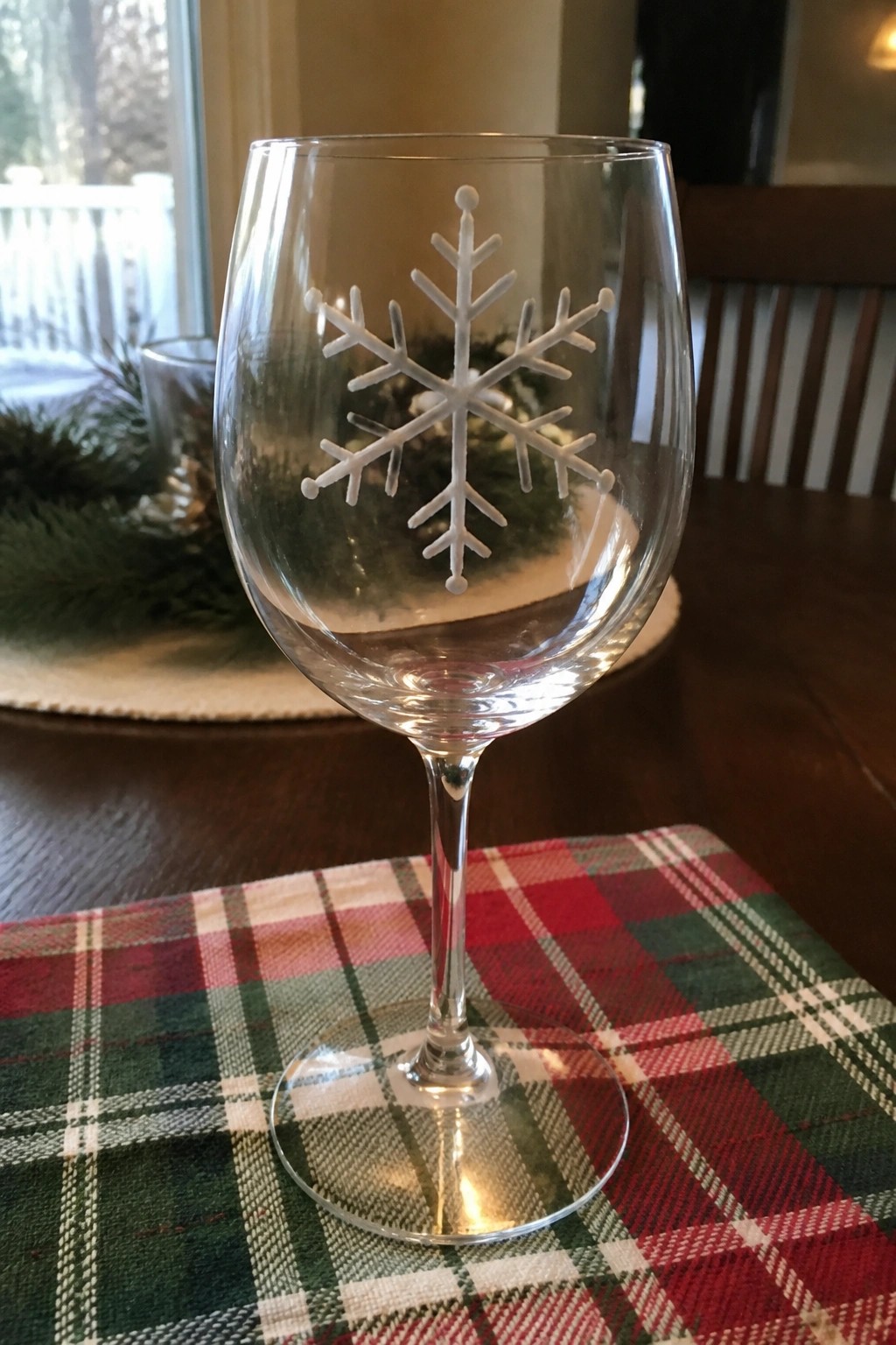 Clear wine glass with etched snowflake on red green plaid tablecloth