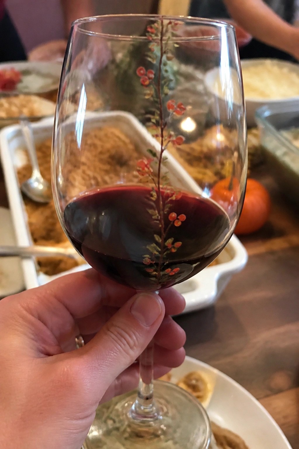 Hand holding wine glass of red wine with red berry design on it