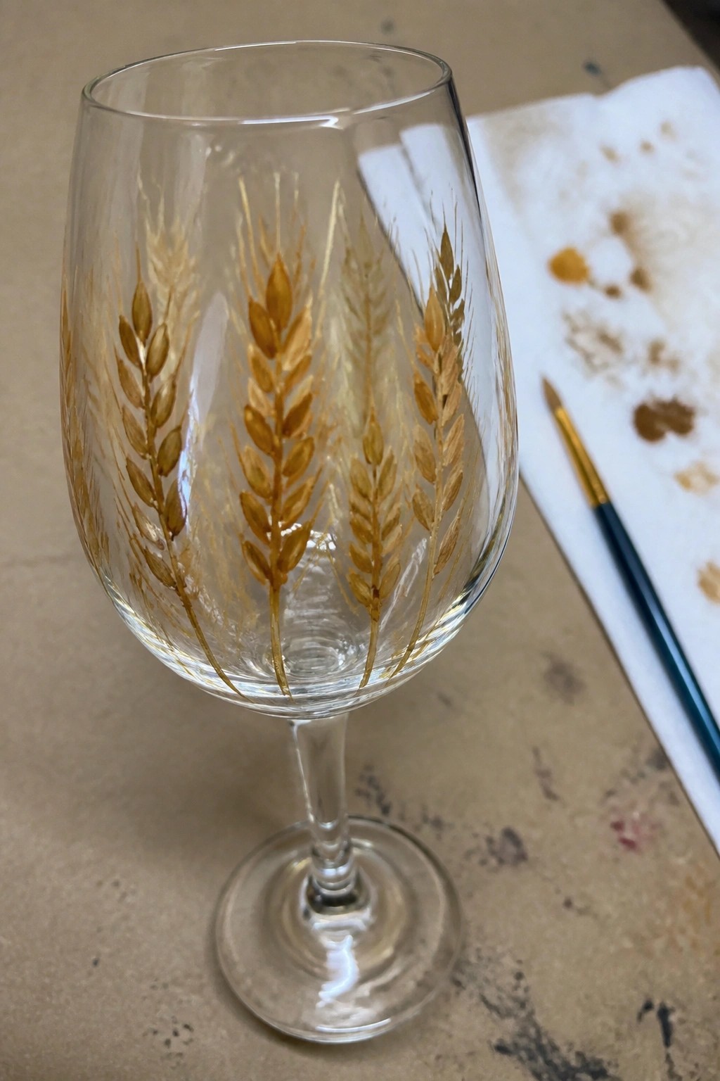 Wine glass with gold wheat stalks beside paintbrush and stained paper towel