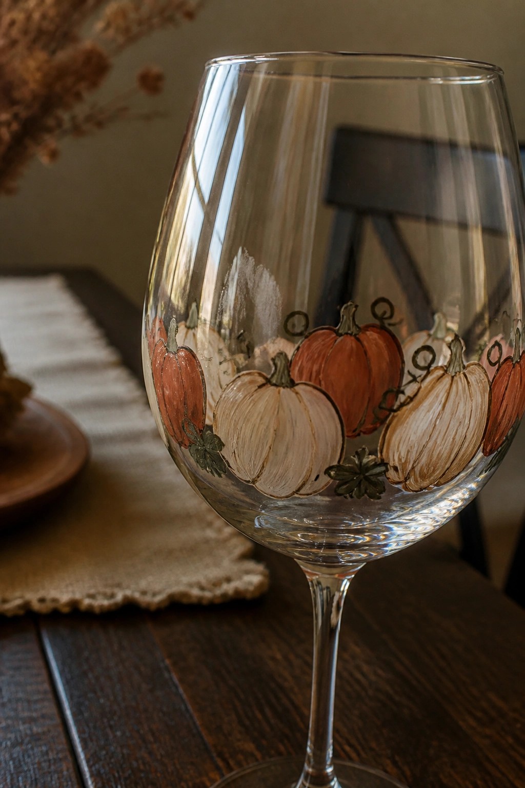 Clear wine glass hand-painted with orange and white pumpkins on wooden table