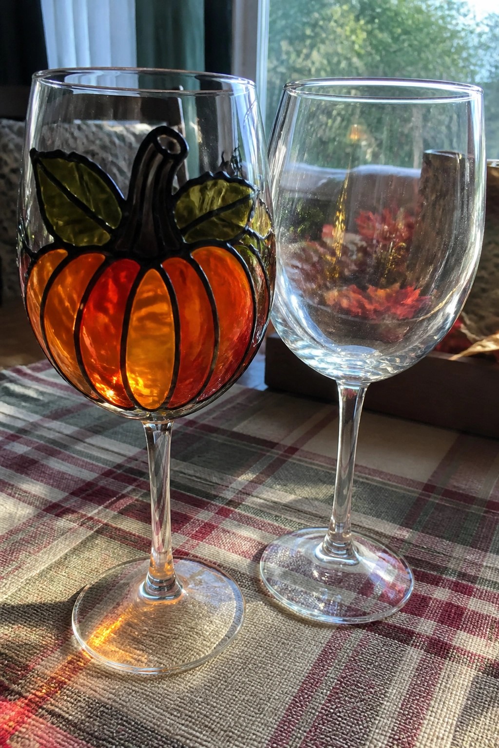 Two wine glasses on plaid cloth, left one with orange pumpkin design.