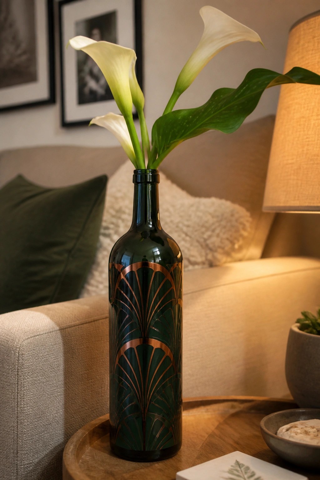 Dark green glass bottle with copper Art Deco pattern holding white calla lilies