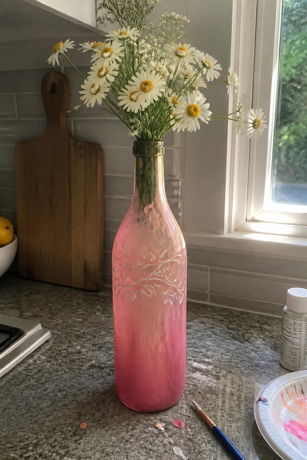 Pink painted bottle vase with white daisies on kitchen counter