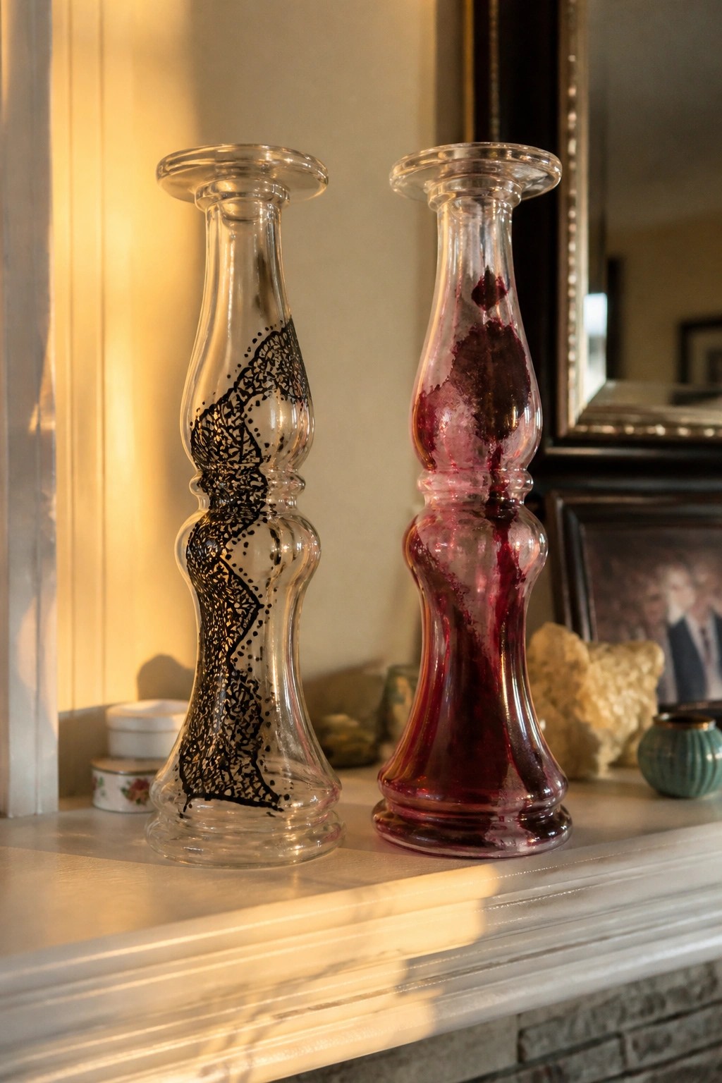 Two ornate glass vases on mantel, one black-patterned and one red-stained.
