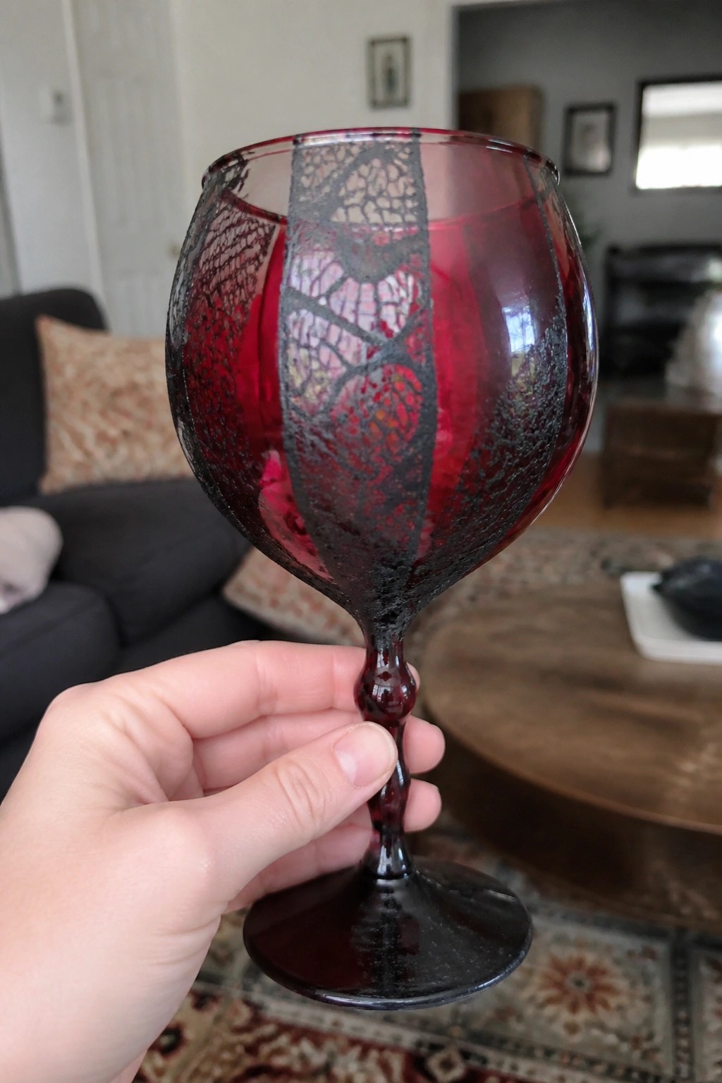 Hand holding red glass goblet with black crackled lace patterns on stem