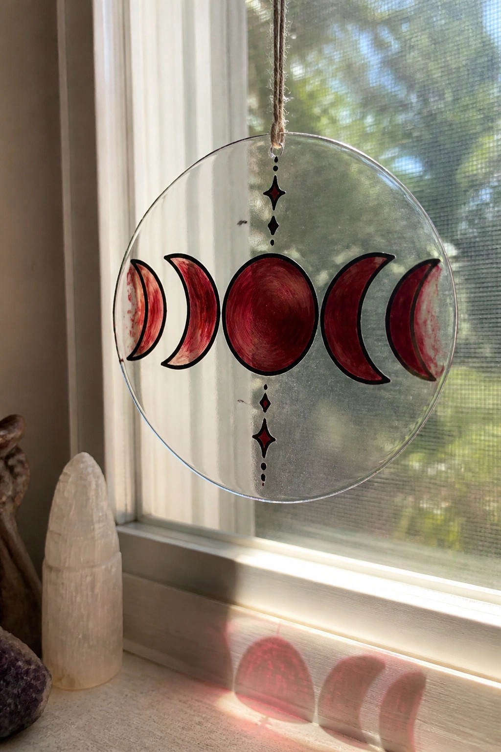 Round glass ornament with red moon phases hanging before sunny window