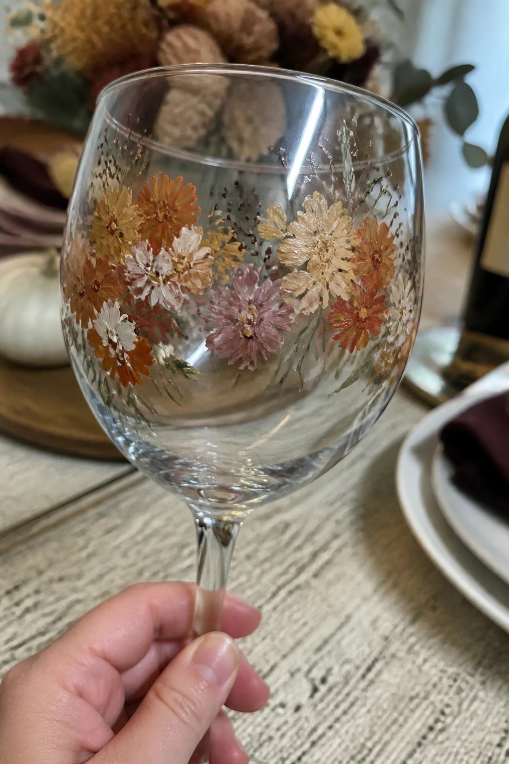 Hand holding wine glass painted with orange, pink, and white flowers