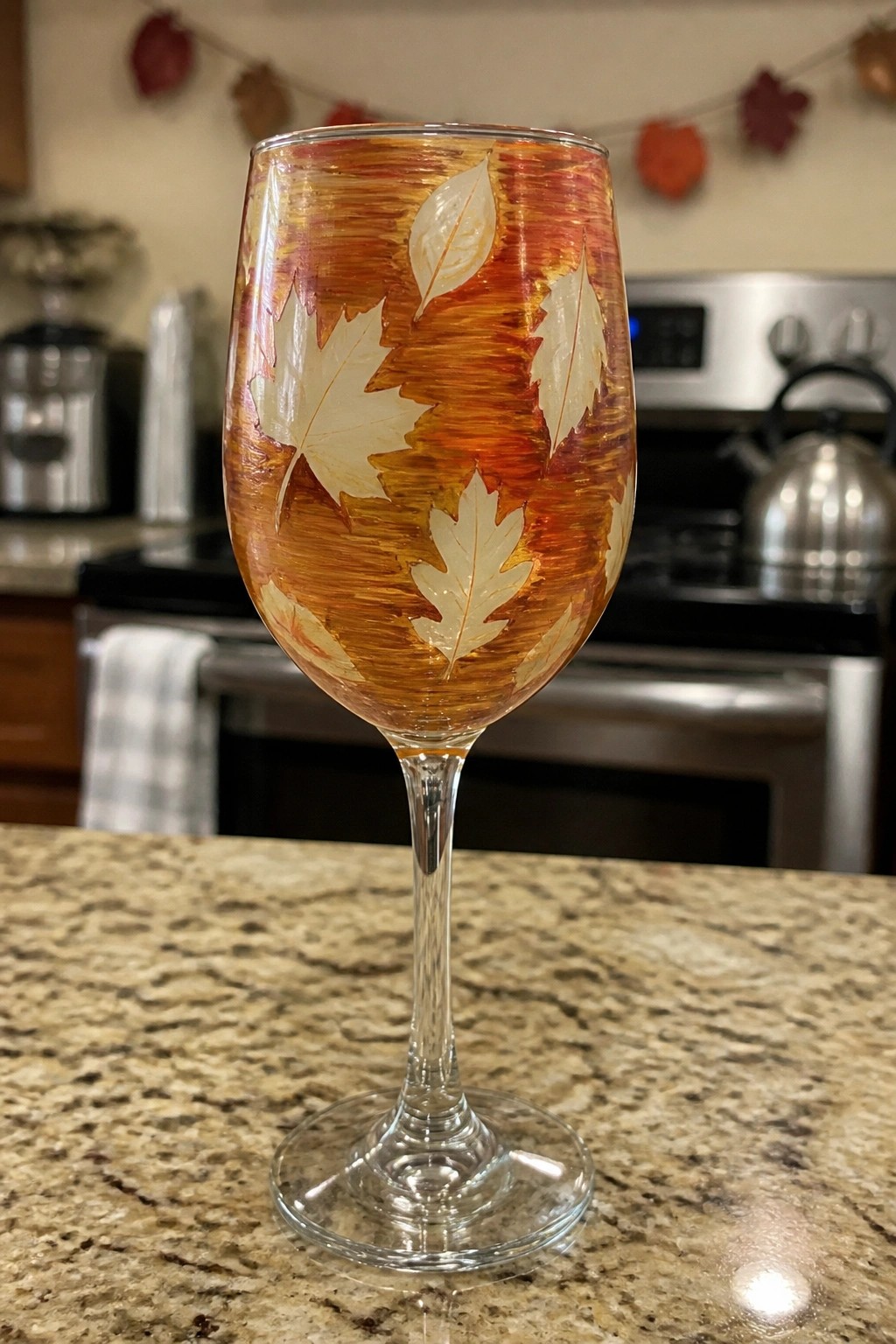 Autumn wine glass with painted orange leaves on granite kitchen counter.