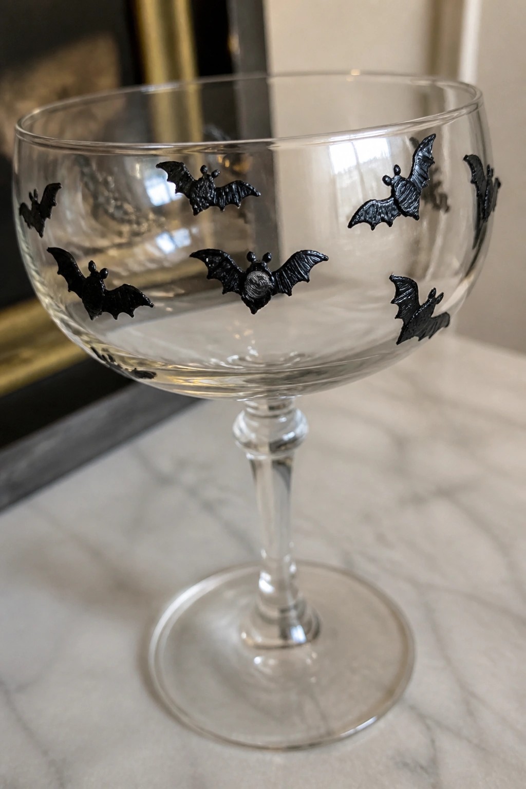Clear coupe glass with black bat decorations on marble surface.