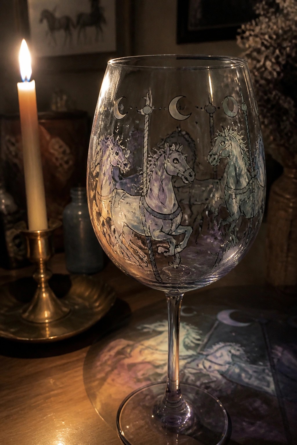 Etched wine glass with purple carousel horses beside a lit candle on wood table