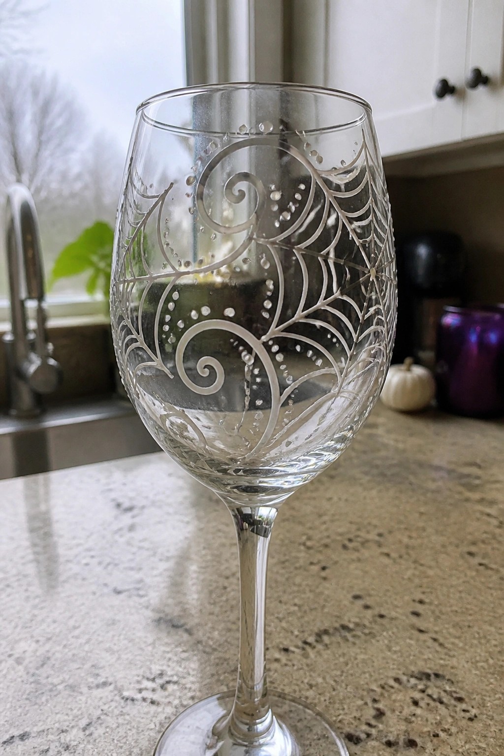 Etched clear wine glass with spiderweb swirls on speckled kitchen countertop