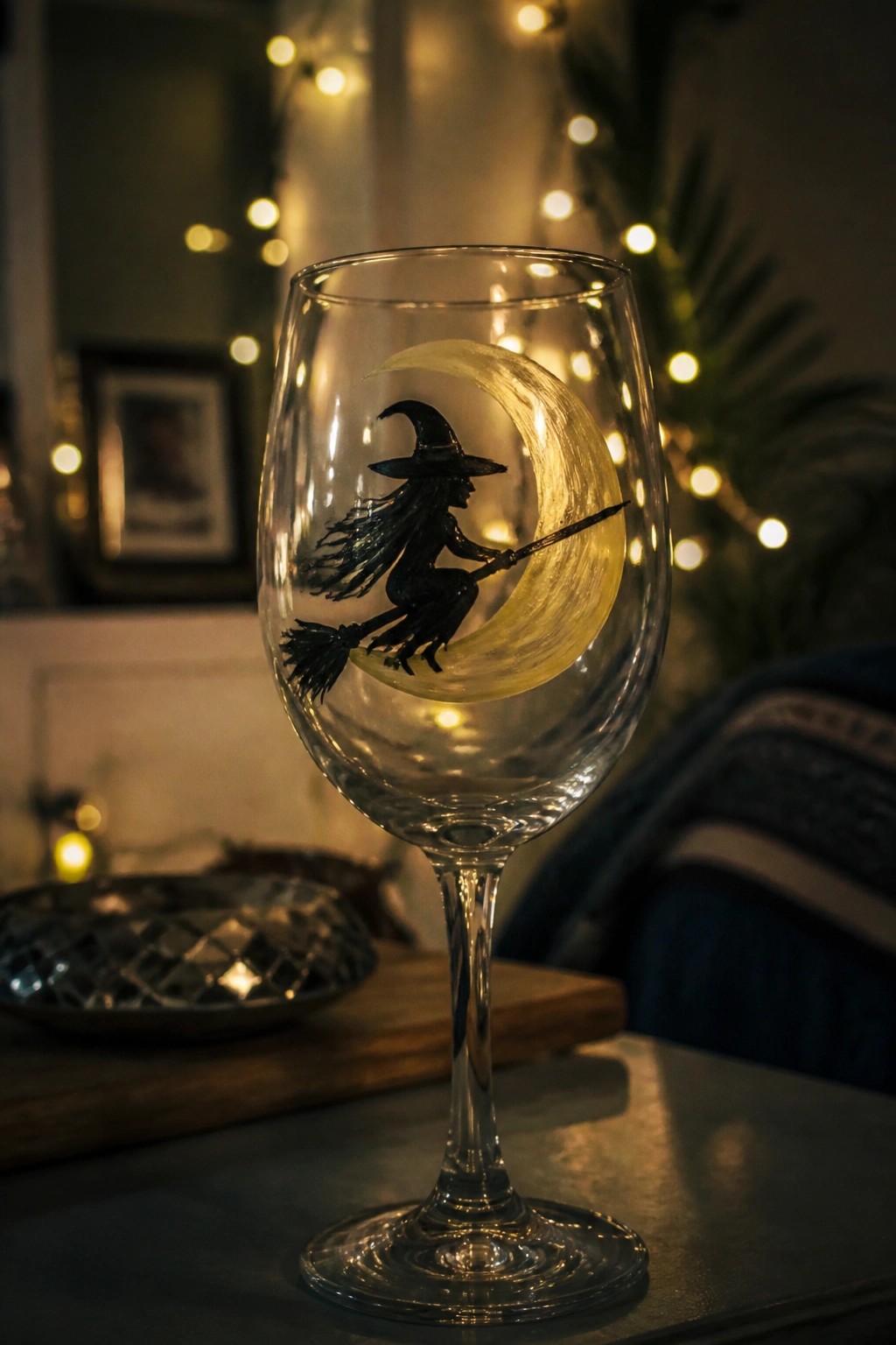 Wine glass with black witch silhouette on broom over glowing yellow crescent moon