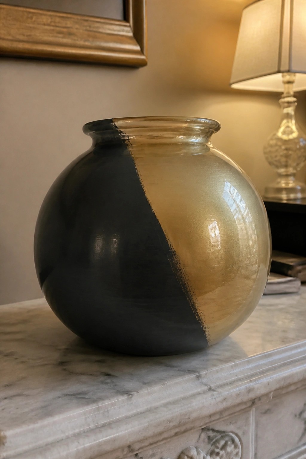 Spherical glass vase painted half black half gold on marble surface