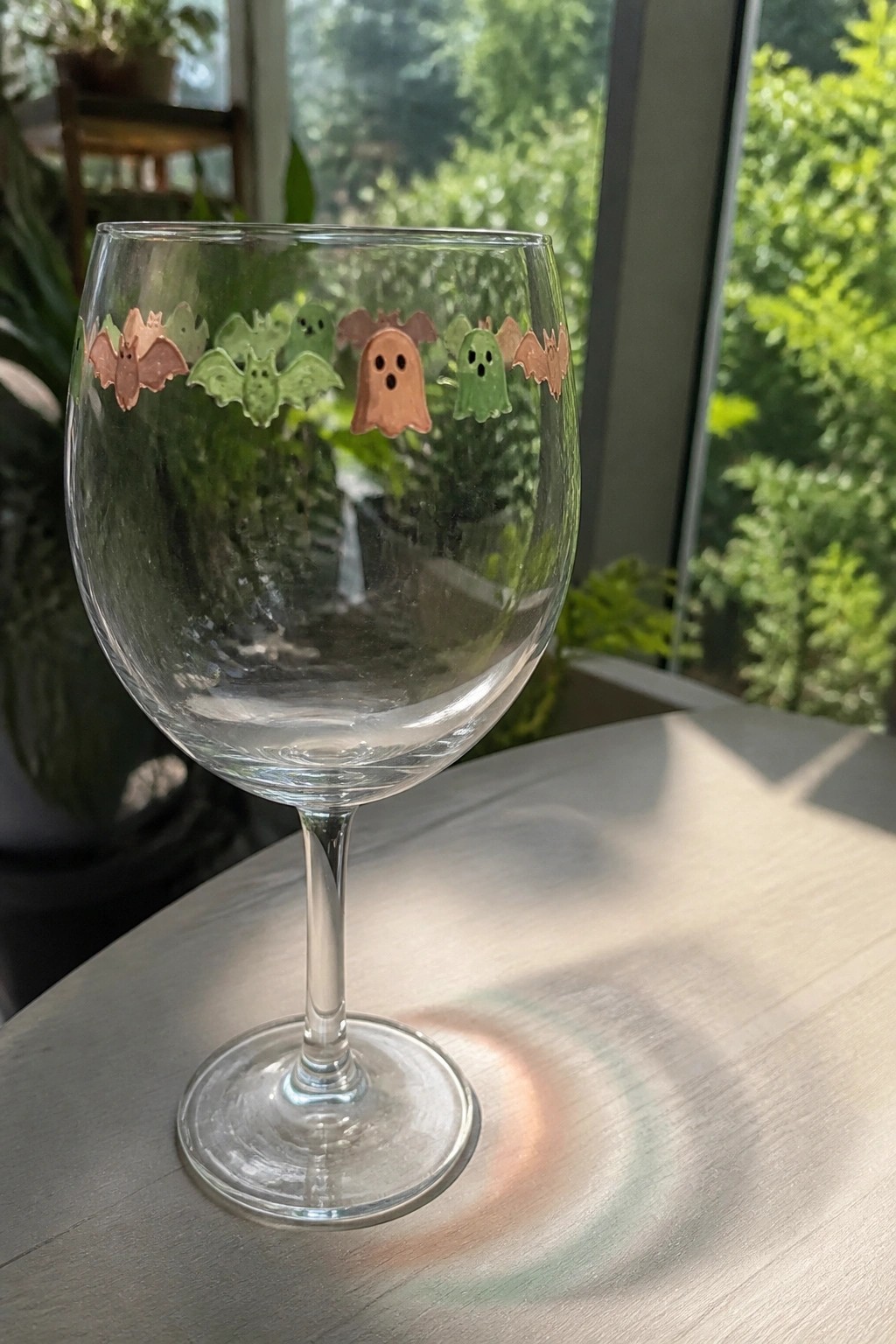 Wine glass with colorful Halloween ghost and bat stickers on sunlit wooden table
